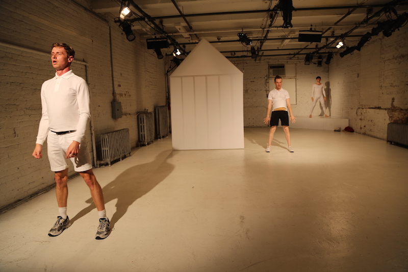 Three men stagger throughout the white chocolate factory stage looking out to the audience